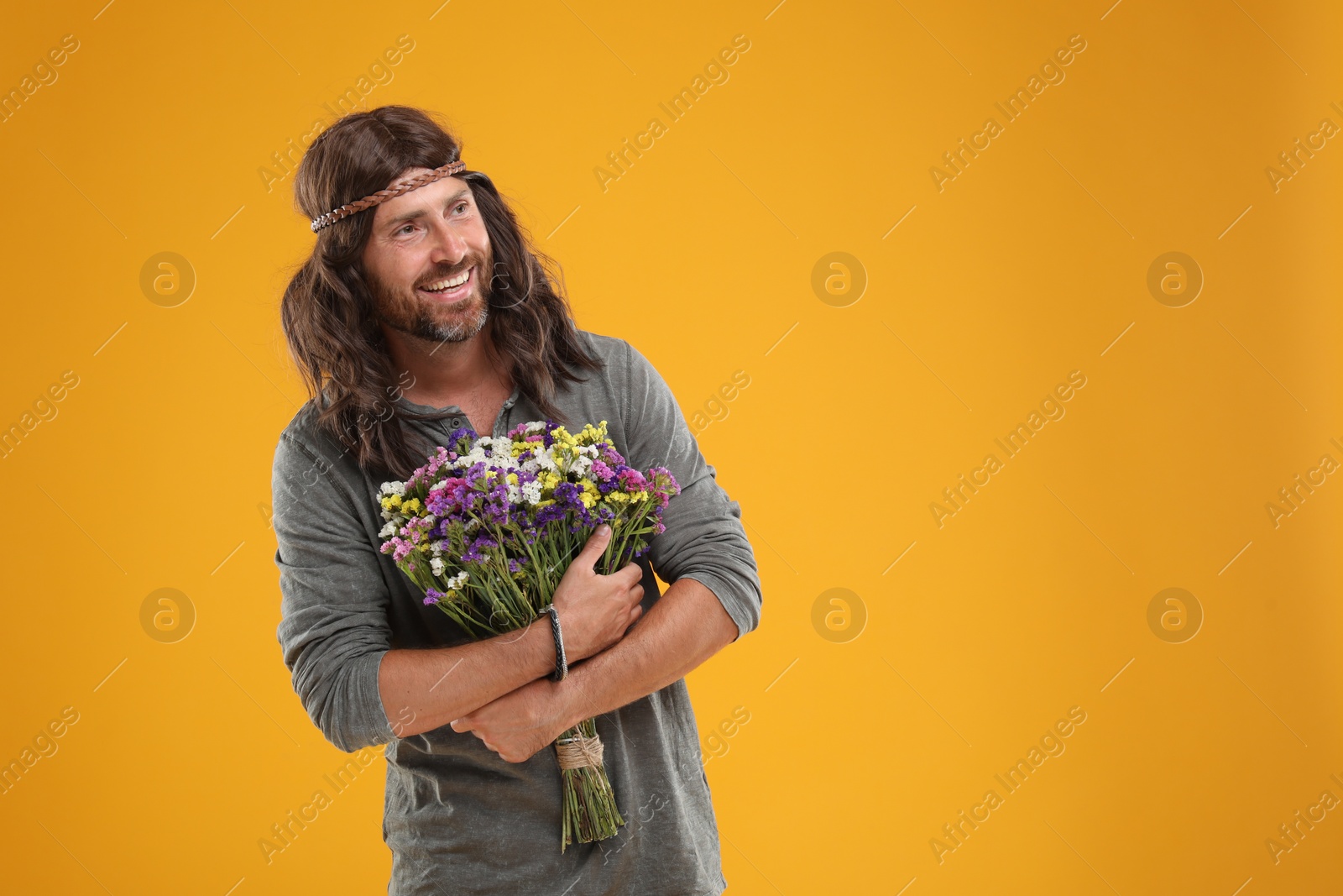 Photo of Hippie man with bouquet of colorful flowers on orange background, space for text