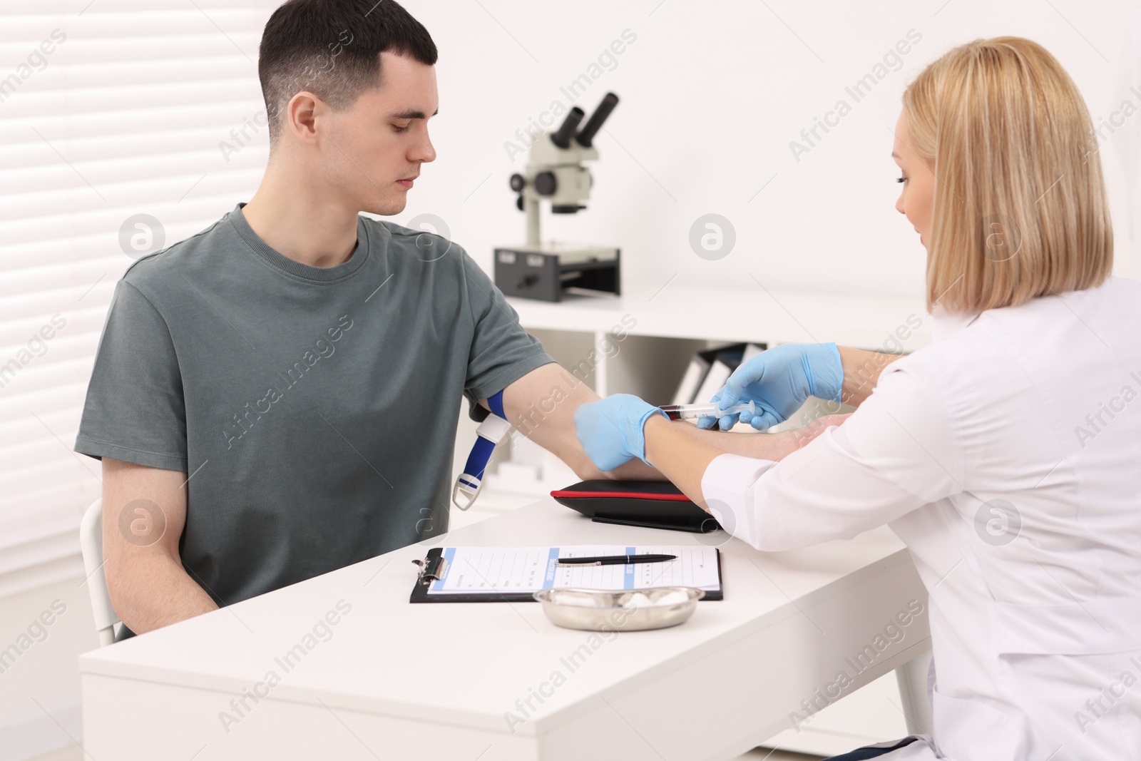 Photo of Doctor taking blood sample from patient with syringe at white table in hospital