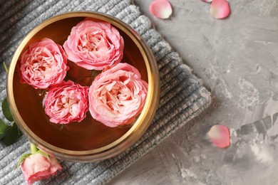 Photo of Tibetan singing bowl with water and beautiful roses on grey textured table, top view. Space for text