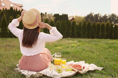 Photo of Young woman having picnic outdoors on summer day, back view