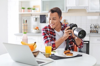 Photo of Portrait of food blogger with laptop and camera in kitchen. Online broadcast