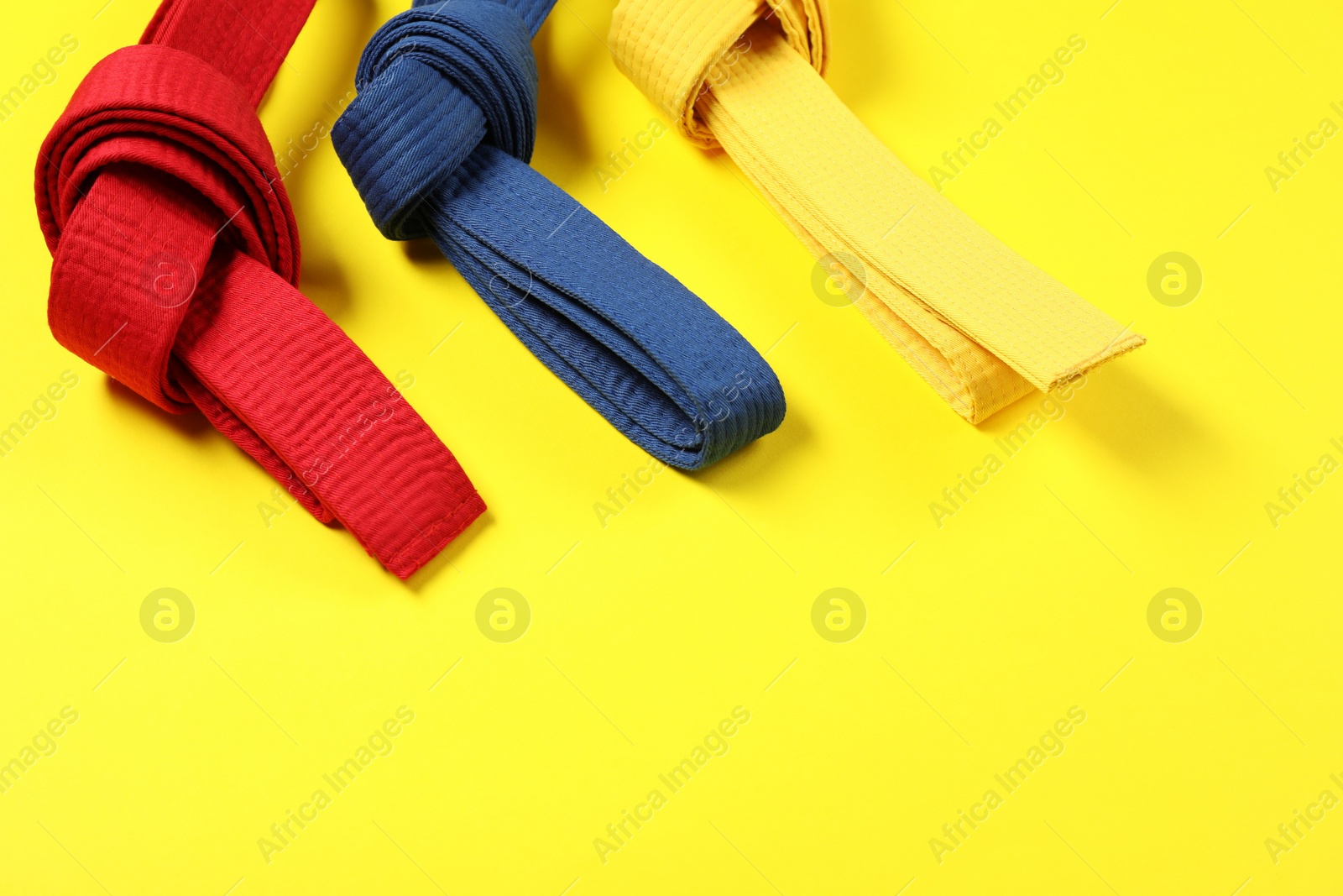 Photo of Colorful karate belts on yellow background, space for text