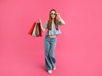 Beautiful young woman with paper shopping bags on pink background
