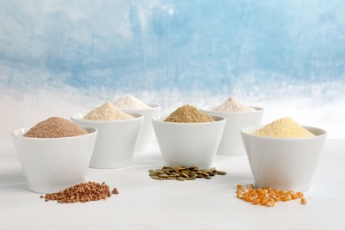 Bowls with different types of flour and seeds on table against color background. Space for text