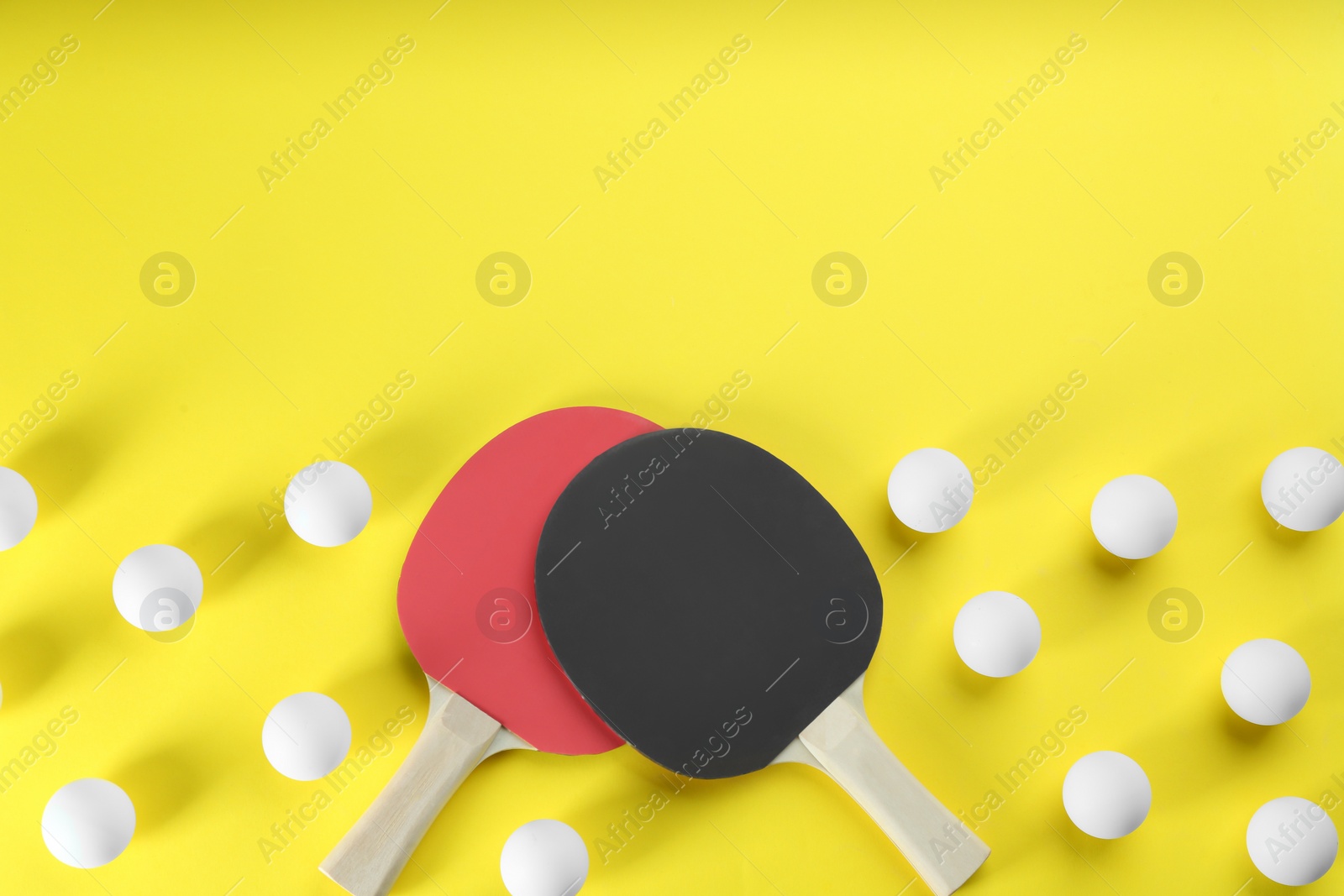 Photo of Ping pong rackets and balls on yellow background, flat lay. Space for text