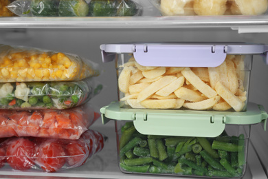 Photo of Plastic bags and containers with different frozen vegetables in refrigerator, closeup