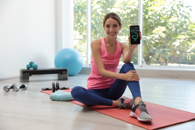 Photo of Young woman showing smartphone with fitness app indoors
