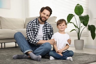 Photo of Happy dad and son sitting on carpet at home