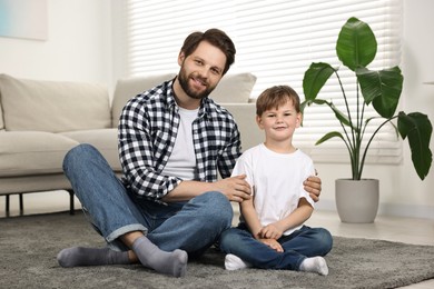 Happy dad and son sitting on carpet at home