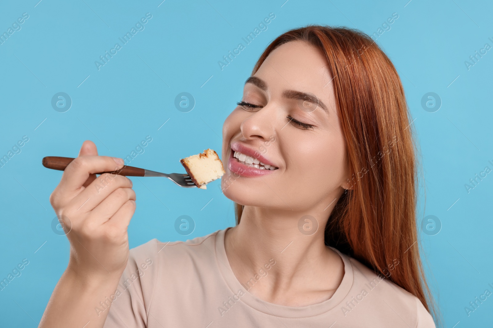 Photo of Young woman eating piece of tasty cake on light blue background