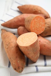 Whole and cut ripe sweet potatoes on kitchen towel, closeup