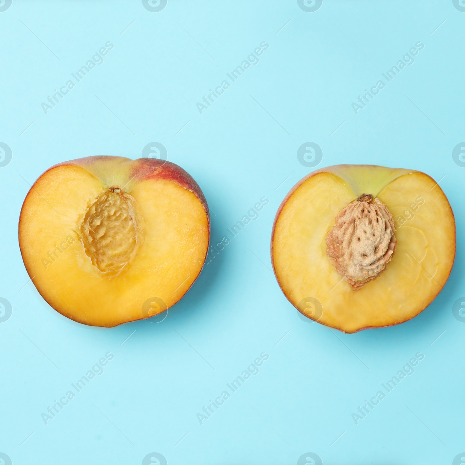 Photo of Halves of sweet juicy peach on light blue background, top view