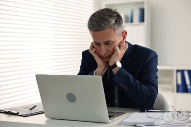 Sleepy man at table with laptop in office