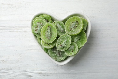 Bowl with slices of kiwi on wooden background, top view. Dried fruit as healthy food