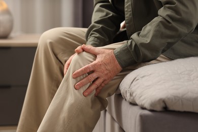 Photo of Senior man suffering from knee pain indoors, closeup. Rheumatism symptom