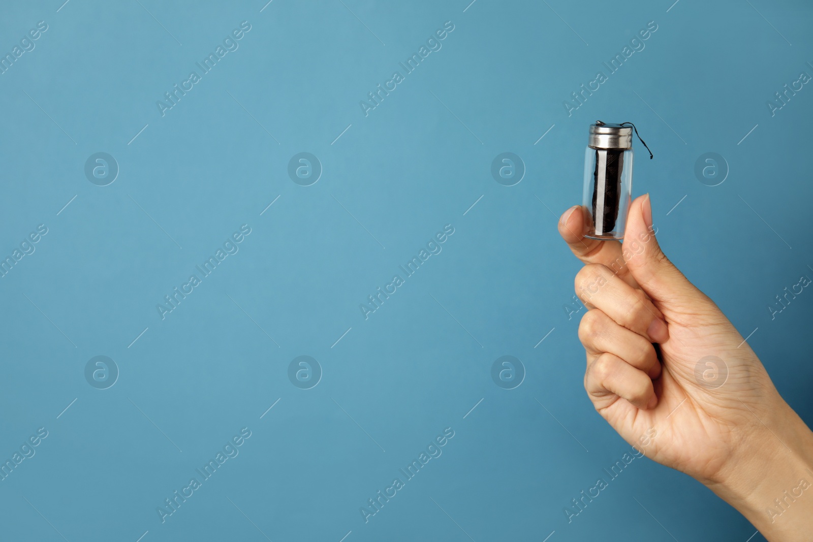 Photo of Woman holding glass jar with biodegradable dental floss against light blue background, closeup. Space for text