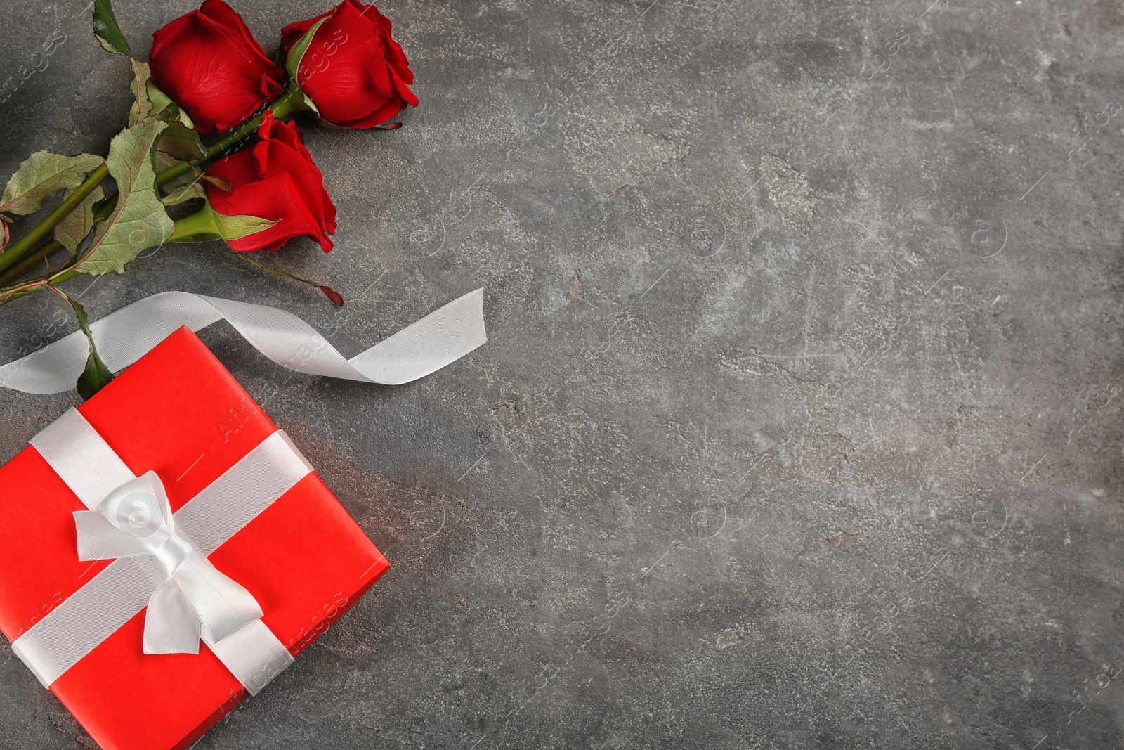 Photo of Beautiful red roses and gift box on grey background, flat lay with space for text. Valentine's Day celebration