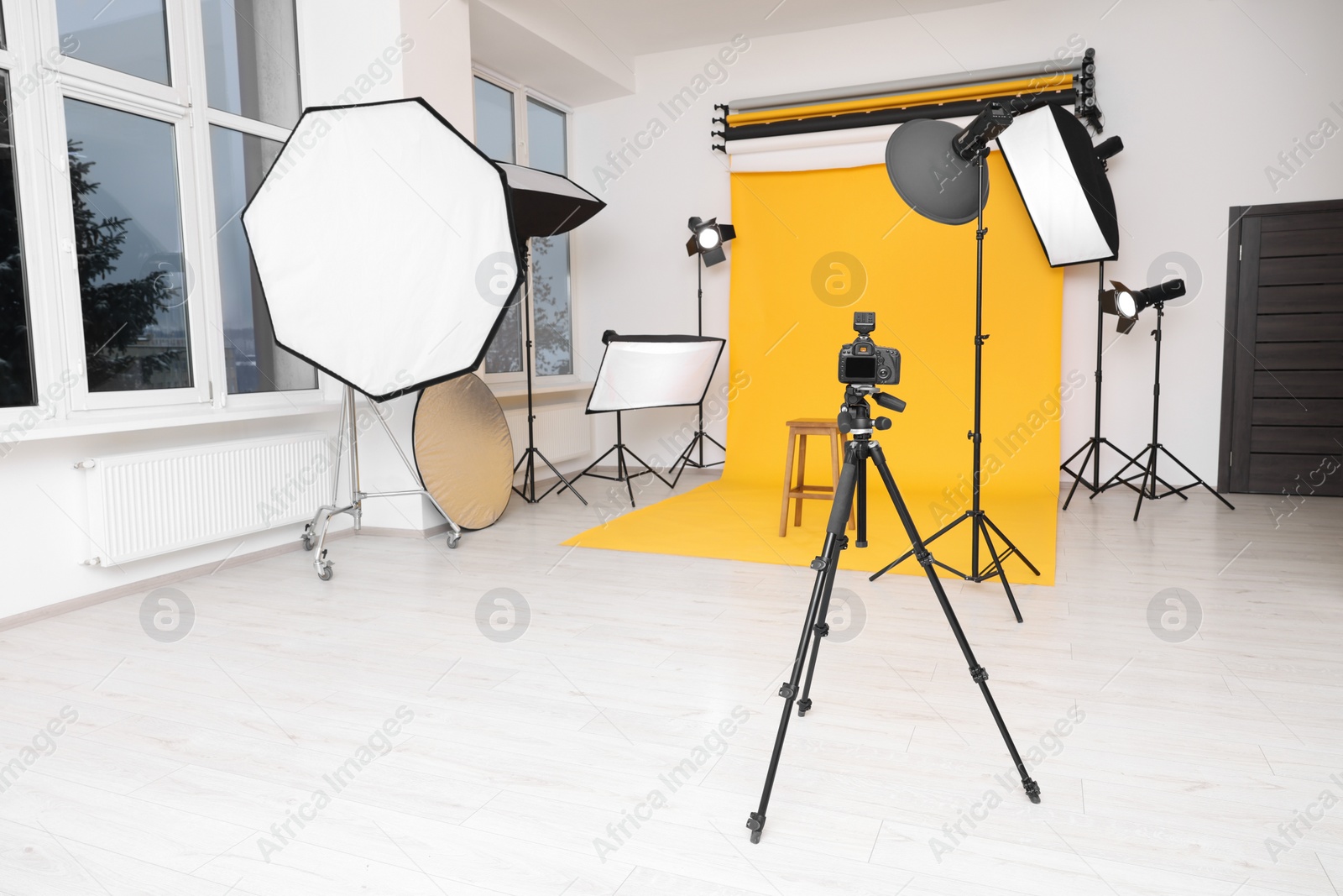 Photo of Camera on tripod, bar stool and professional lighting equipment in modern photo studio