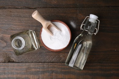 Photo of Vinegar in glass bottles and baking soda on wooden table, flat lay