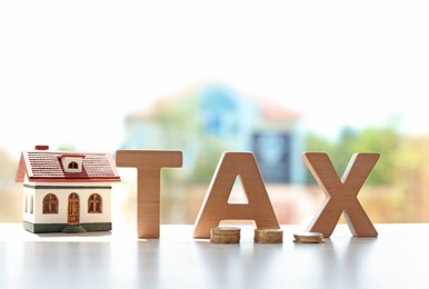 Word TAX, house model and coins on table against blurred background