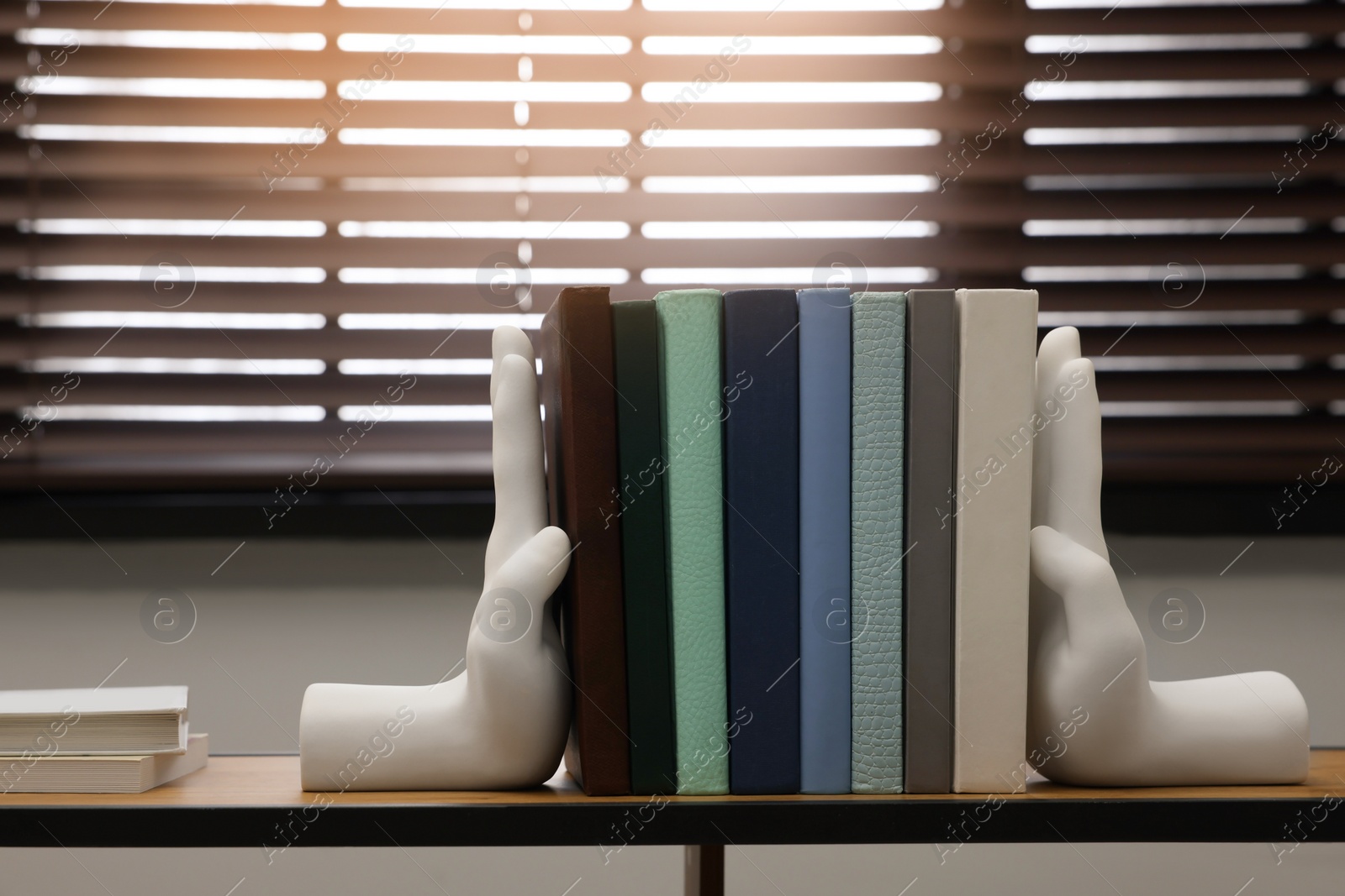 Photo of Beautiful hand shaped bookends with books on shelf indoors