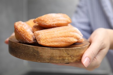 Woman holding wooden board with madeleine cookies, closeup