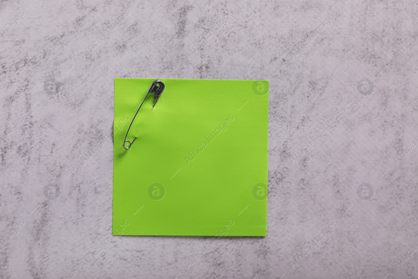 Photo of Green paper note with safety pin on grey textured background, top view