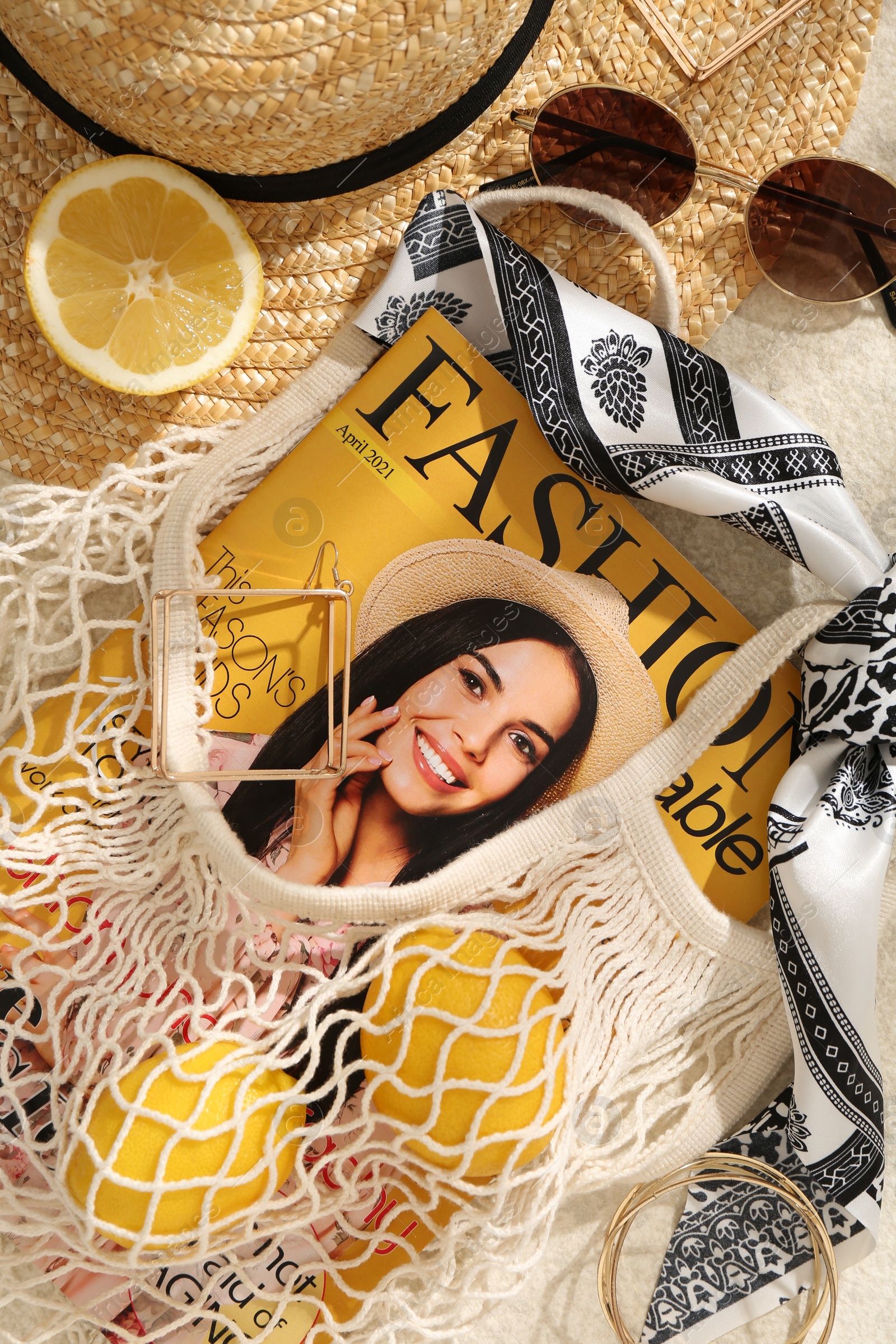 Photo of String bag with fashion magazine, fresh lemons and accessories on beige background, flat lay