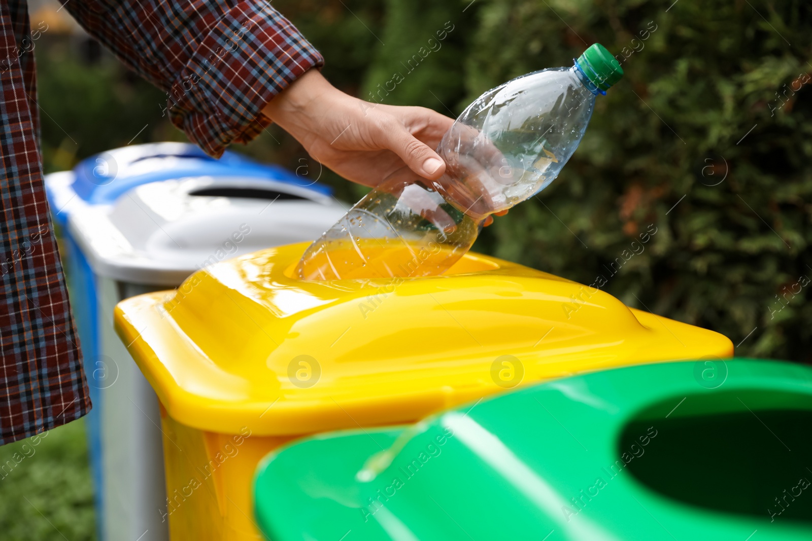 Photo of Woman throwing plastic bottle into recycling bin outdoors, closeup