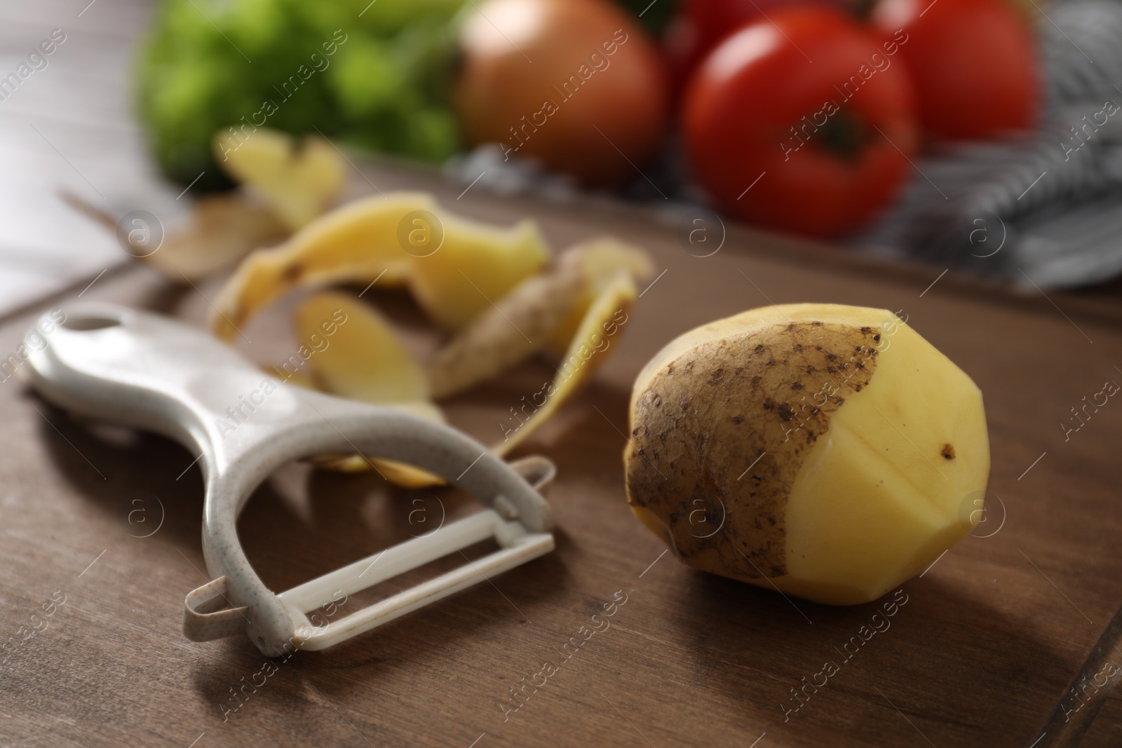 Photo of Wooden board with potato, peels and peeler on table, closeup