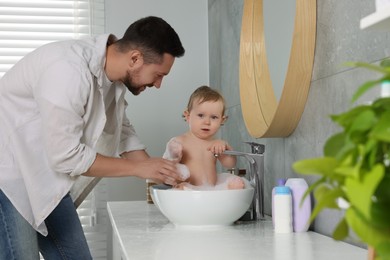 Father washing his little baby in sink at home