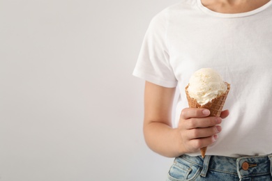Woman holding ice cream in wafer cone on light background, closeup. Space for text