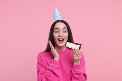 Woman in party hat eating piece of tasty cake on pink background