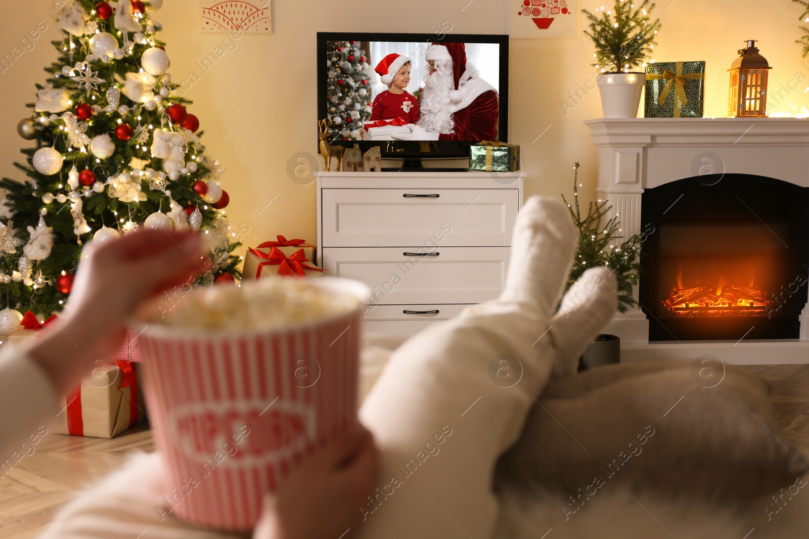 Image of Woman with popcorn watching festive movie on TV in room decorated for Christmas, closeup