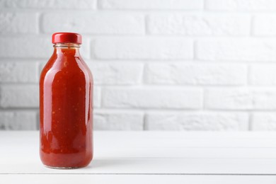 Photo of Spicy chili sauce in bottle on white wooden table, space for text