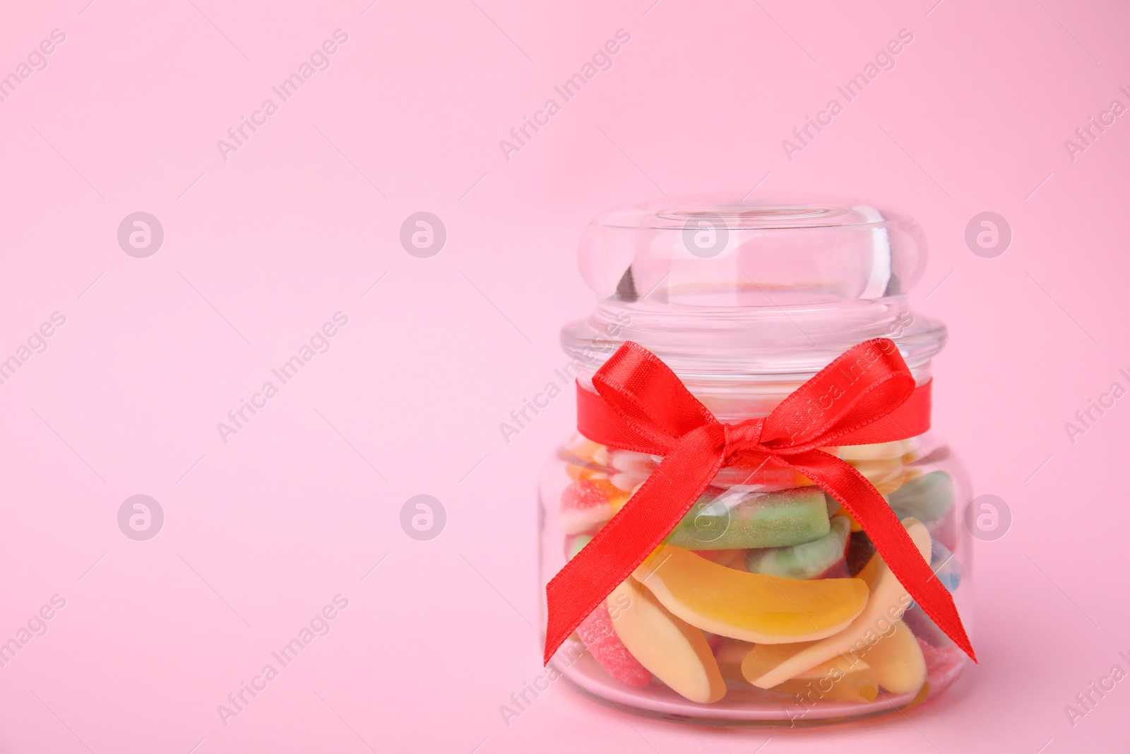 Photo of Tasty colorful jelly candies in glass jar on pink background. Space for text