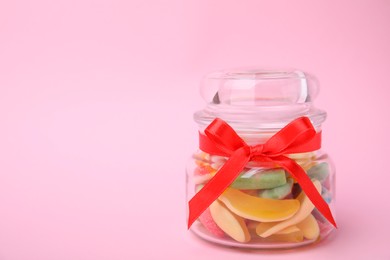 Photo of Tasty colorful jelly candies in glass jar on pink background. Space for text
