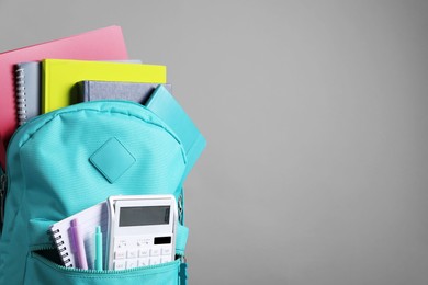 Turquoise backpack and different school stationery on grey background, space for text