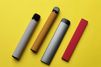 Different electronic cigarettes on yellow background, flat lay