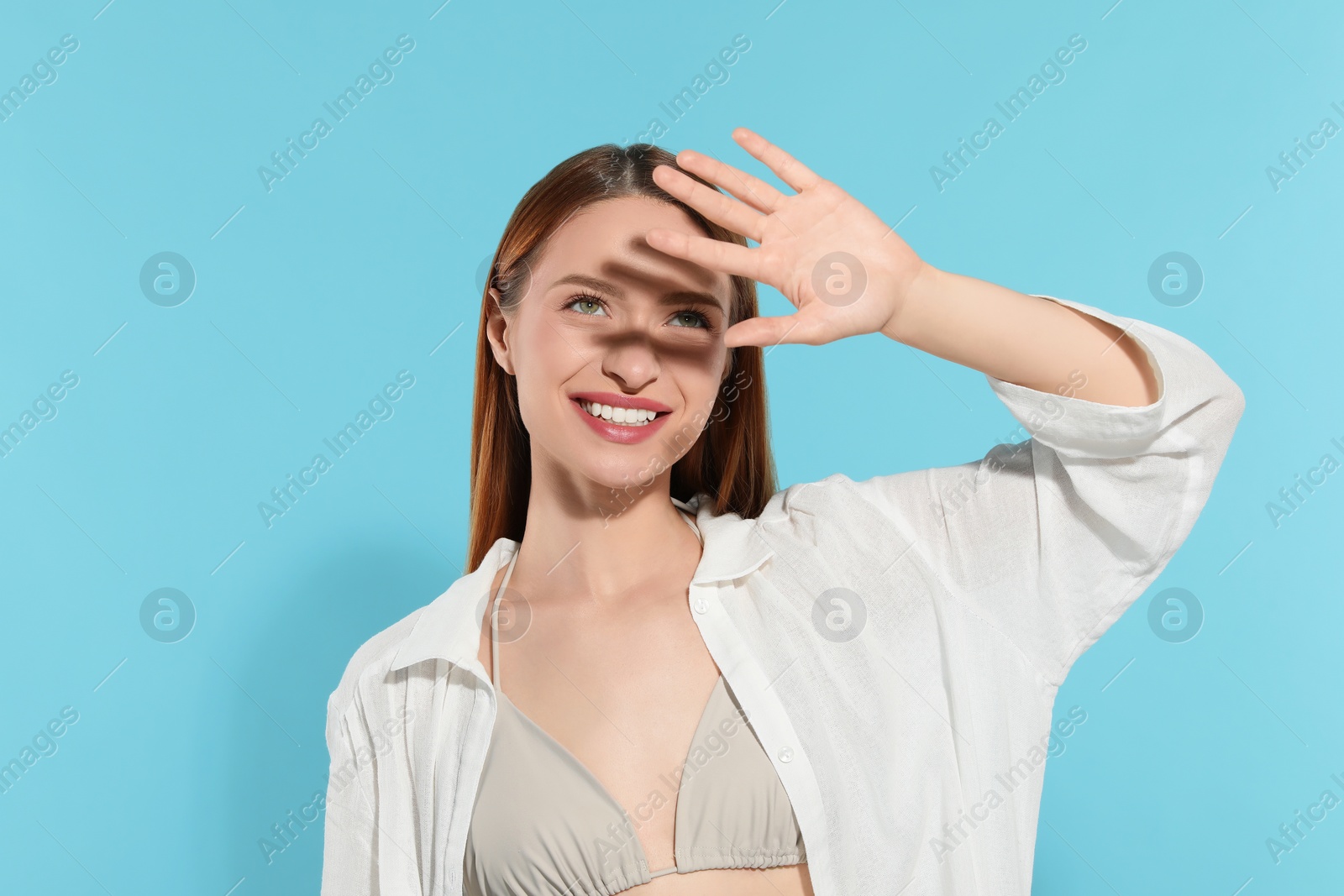 Photo of Beautiful young woman shading herself with hand from sunlight on light blue background