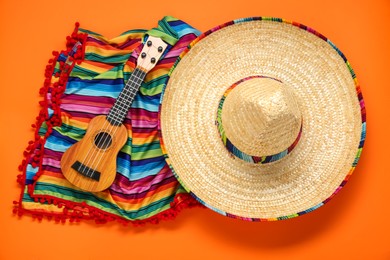Photo of Mexican sombrero hat, guitar and colorful poncho on orange background, flat lay
