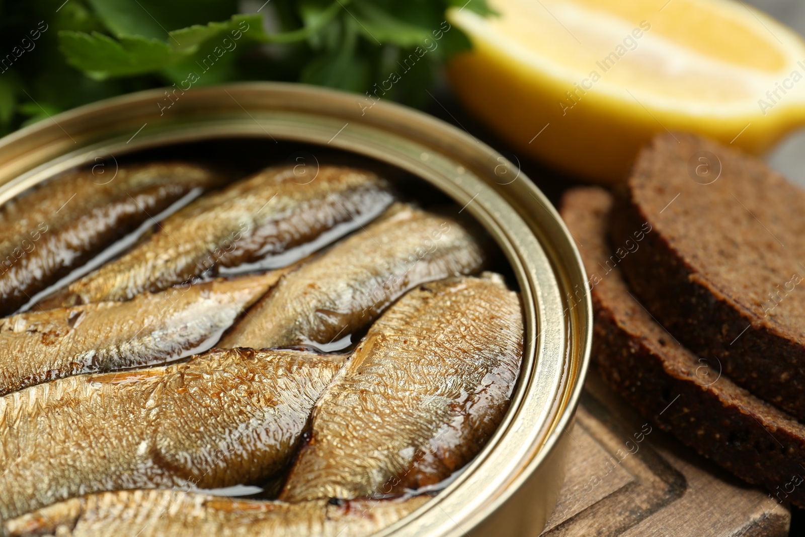 Photo of Tin can with tasty sprats served on wooden board, closeup