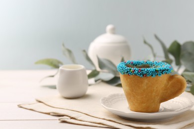 Photo of Delicious edible biscuit coffee cup decorated with sprinkles on white wooden table, space for text