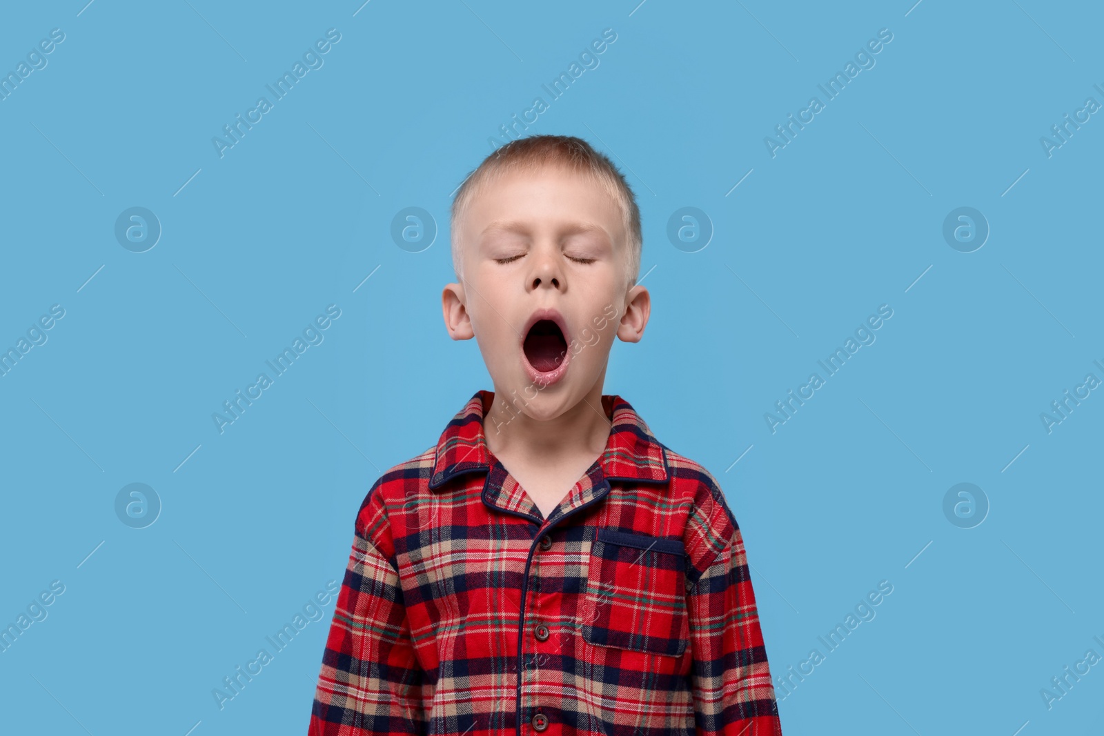 Photo of Sleepy boy yawning on light blue background. Insomnia problem