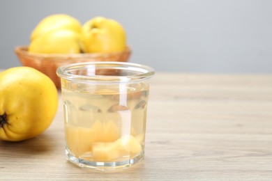 Photo of Delicious quince drink in glass and fresh fruits on wooden table, space for text