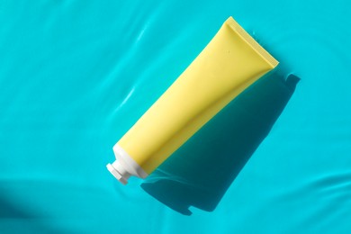 Tube with moisturizing cream in water on light blue background, top view