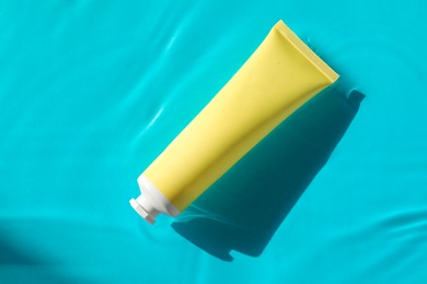 Photo of Tube with moisturizing cream in water on light blue background, top view