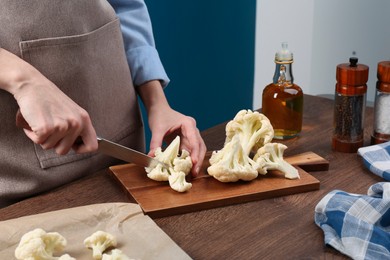 Photo of Woman cutting fresh cauliflower at wooden table, closeup