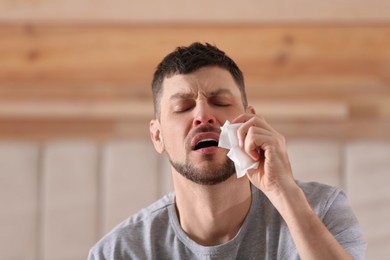 Photo of Ill man with paper tissue sneezing at home