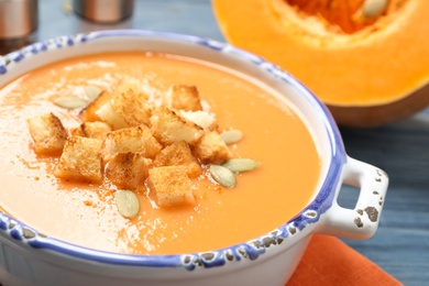 Photo of Tasty creamy pumpkin soup with croutons and seeds in bowl on table, closeup
